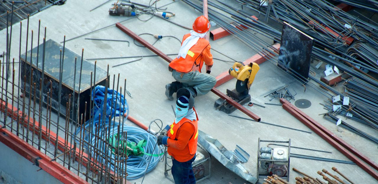 Construction worker standing on a concrete surface surrounded by metal poles and another construction worker