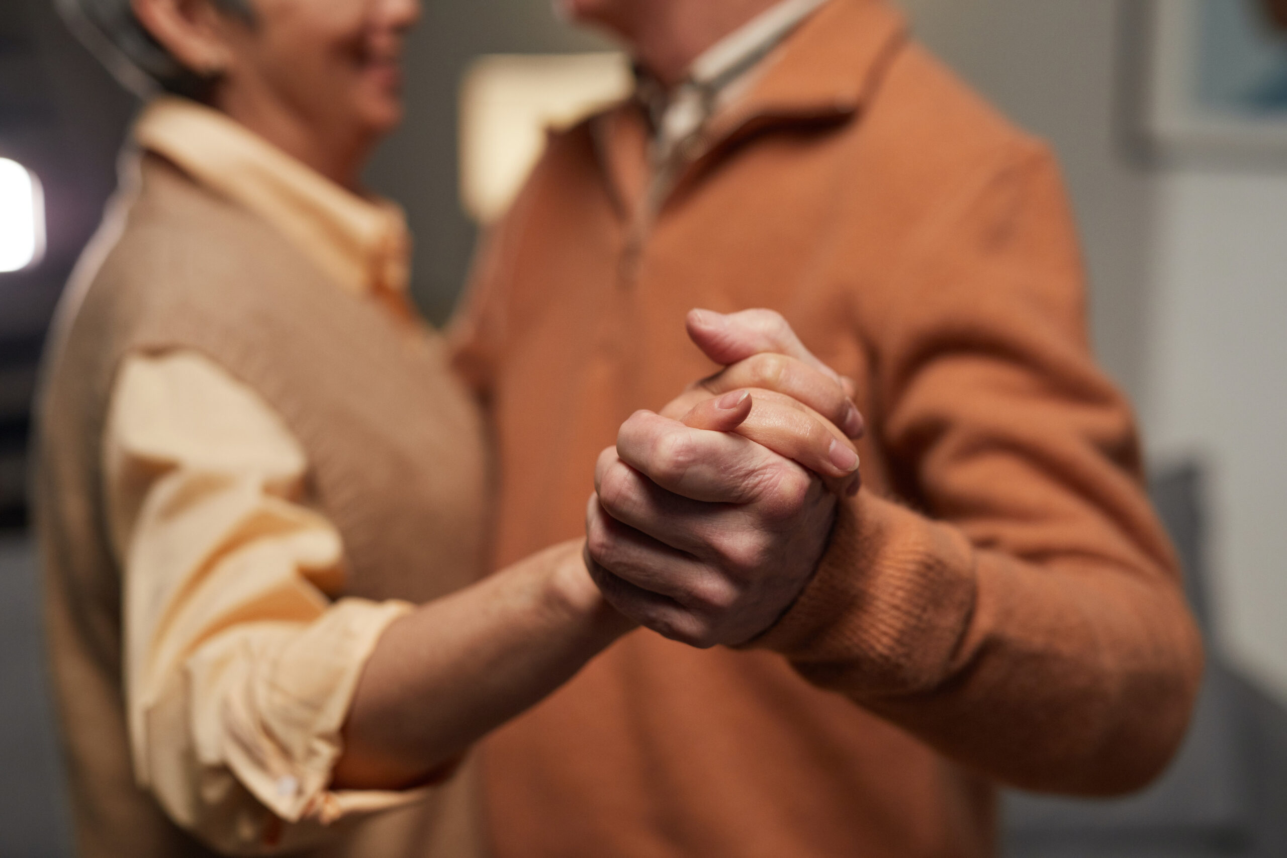 Close up of an older couple dancing, with the woman in a yellow shirt and brown vest and the man in an orange pullover